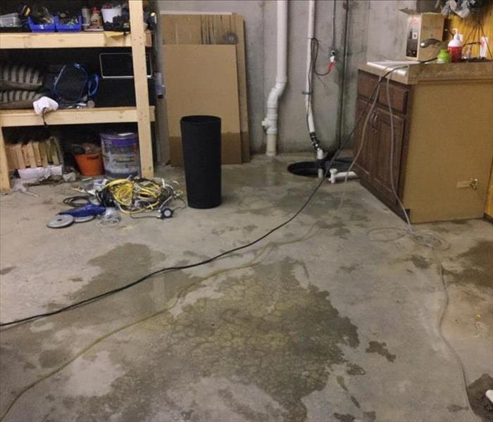 it is a section of a residential garage with shelving and there is water on the floor.