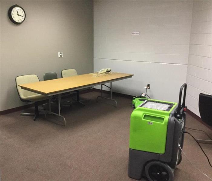 The same conference room with wet carpet has a green SERVPRO fan and dehumidifier in it to dry the affected area