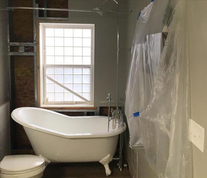 A small bathroom with a claw foot tub and a sheet of plastic on the wall has water damage