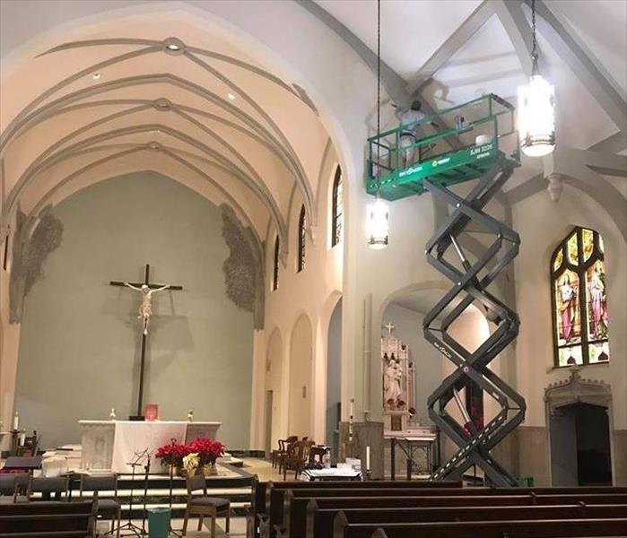 The rectory space of a church has a lift going all the way to the ceiling with a worker on it cleaning the ceiling 