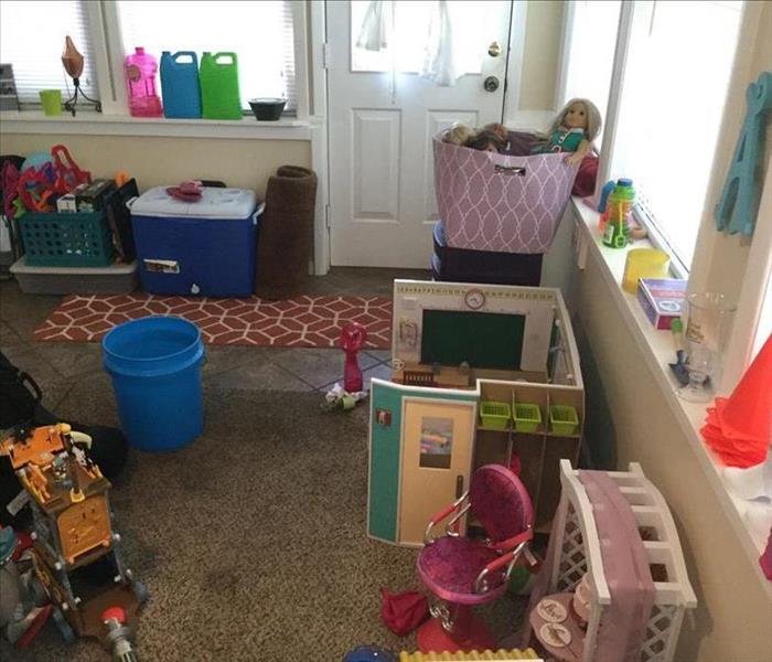 A small room full of toys has a bucket on the floor to catch the water that is coming in from the ceiling above