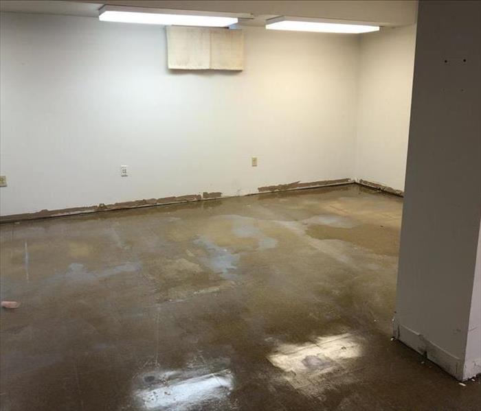 A large empty room in a commercial building has water covering the floor