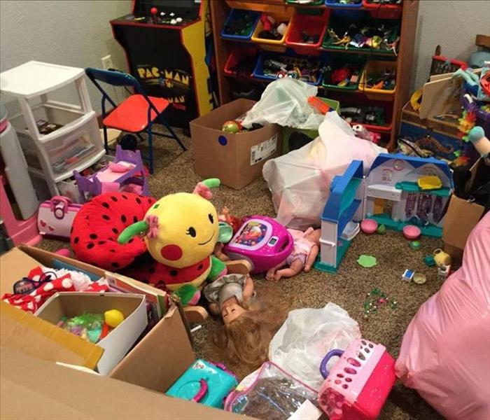 A small room in a basement is carpeted and full of children's toys. The carpet is wet from a water loss